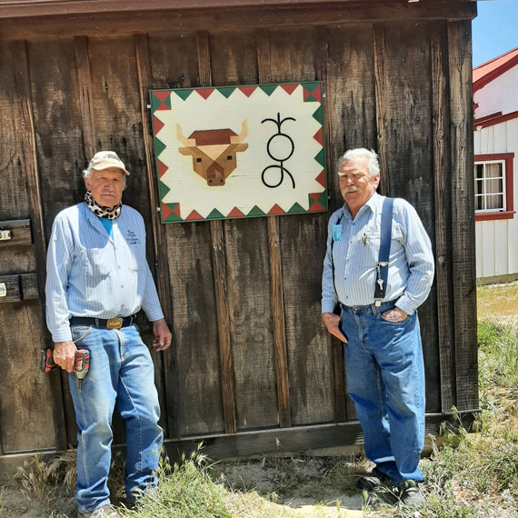 Photo of craftsmen Don Simon, left, and Rick Barr stand with the intricate wooden barn quilt they designed